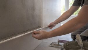 Ein Fliesenleger bringt im Badezimmer eine Eckschiene für den sauberen Abschluss des Putzes an.