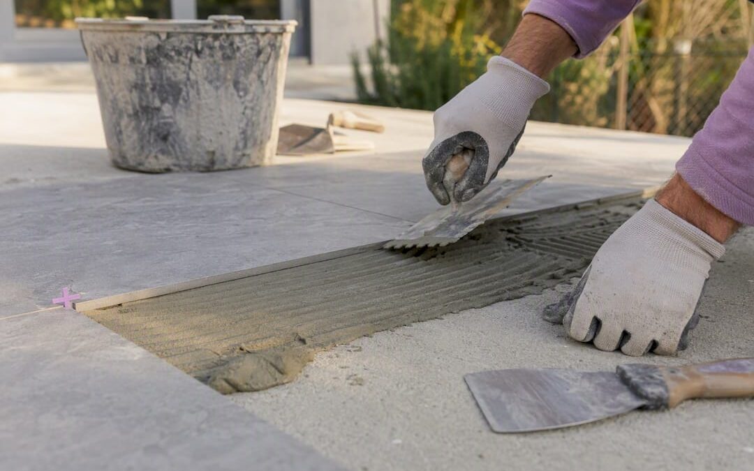 Nahaufnahme von Händen, die Kleber auf eine Terrassenfliese auftragen