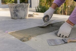 Nahaufnahme von Händen, die Kleber auf eine Terrassenfliese auftragen