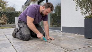 Heimwerker erneuert die Fugen einer Terrasse mit einem Fugenschaber