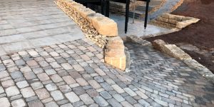 Einfahrt mit Pflastersteinen, Kiesstreifen und Natursteinblöcken im modernen Außenbereich