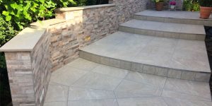 Moderner Hauseingang mit breiten Stufen, großformatigen Außenfliesen und Natursteinwand