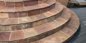 Halbrunde Außentreppe mit Natursteinplatten in warmen Rot- und Orangetönen