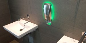 Modernes Sanitärbereich im Gewerbe mit grauen Wandfliesen und beleuchtetem Seifenspender